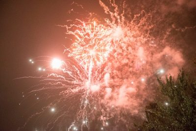 Red and orange fireworks in a night sky with green trees in the foreground